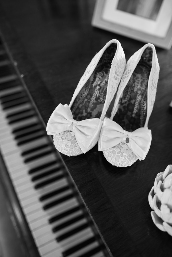 Black and white photo of lace bridal shoes with bows on piano keys