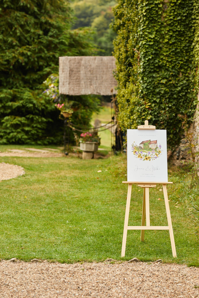 Wedding welcome sign on an easel on the lawn at the Lost Village of Dode