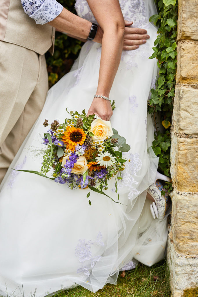 Close-up of the bride's wildflower bouquet against her dress with the groom's hand at her waist