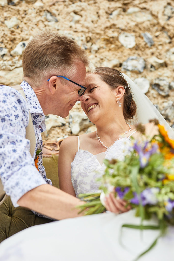 Bride and groom laughing forehead to forehead against a flint wall at the Lost Village of Dode
