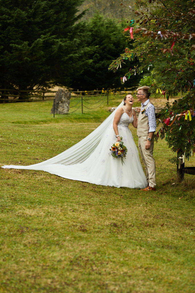 Bride and groom on the lawn at the Lost Village of Dode with her long veil trailing across the grass