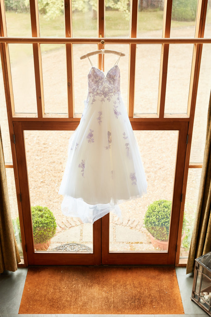 Wedding dress embroidered with blue flowers hanging in a glazed doorway