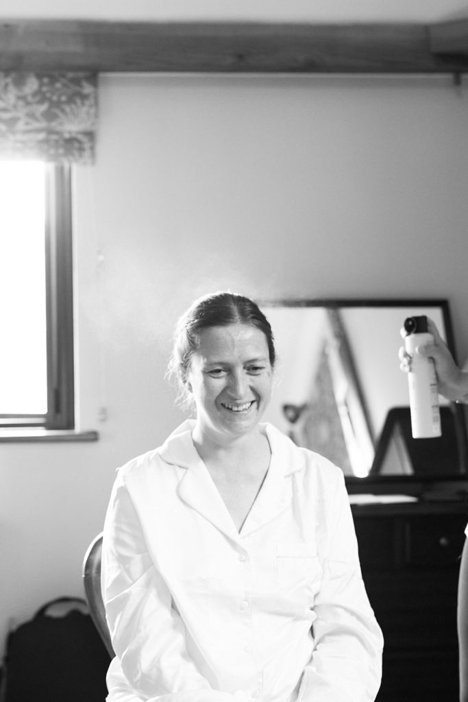 Black and white photo of the bride smiling in a white shirt as she gets ready