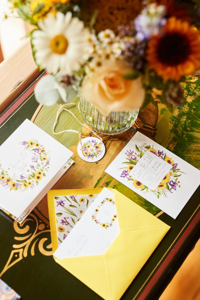 Wedding stationery with a wildflower wreath design beside a vase of flowers