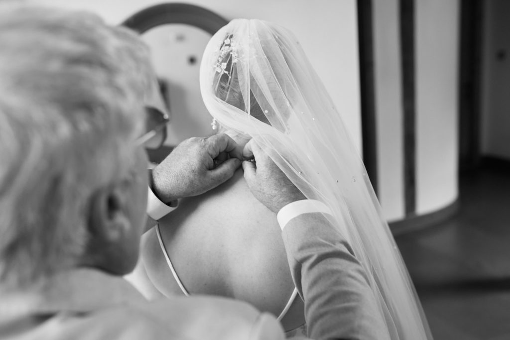 Black and white photo of a man fastening the bride's necklace