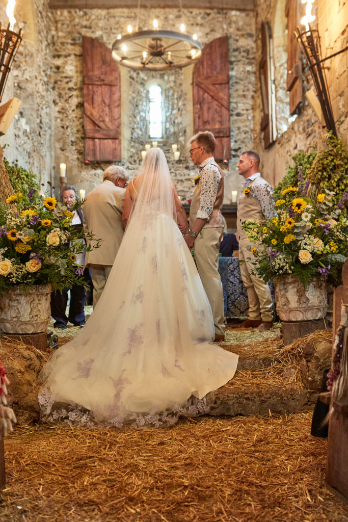Bride and groom at the front of the church at Dode, seen from behind across the straw-covered floor