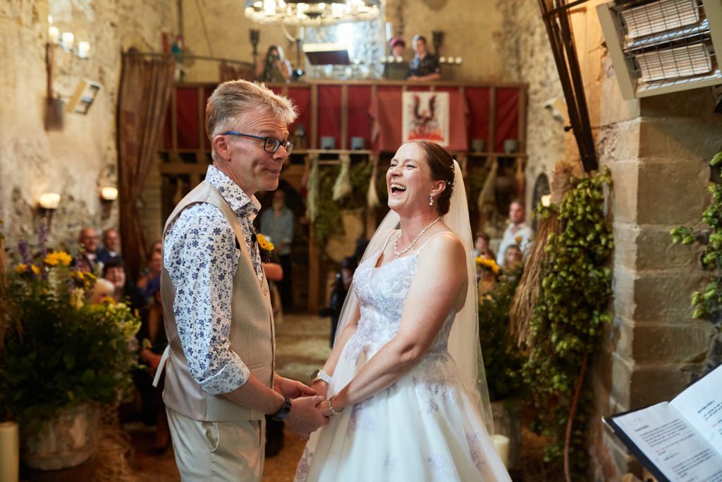 Bride and groom holding hands as they say their vows in the church at Dode