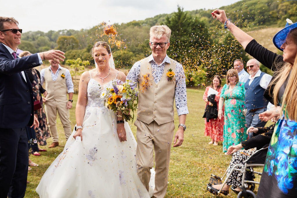 Bride and groom walking through confetti on the lawn at the Lost Village of Dode