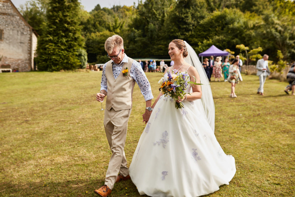 Bride and groom walking hand in hand across the lawn at the Lost Village of Dode