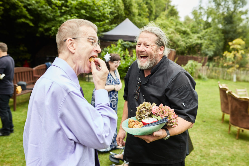Groom laughing with a caterer as he tries a canapé