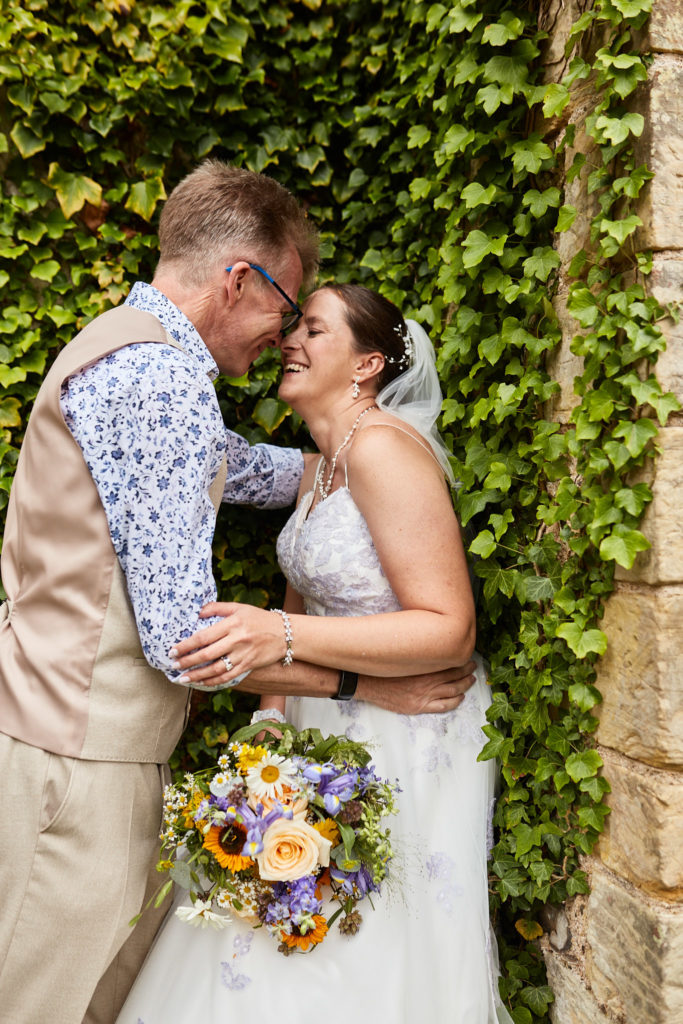 Bride and groom nose to nose against an ivy-covered wall at the Lost Village of Dode