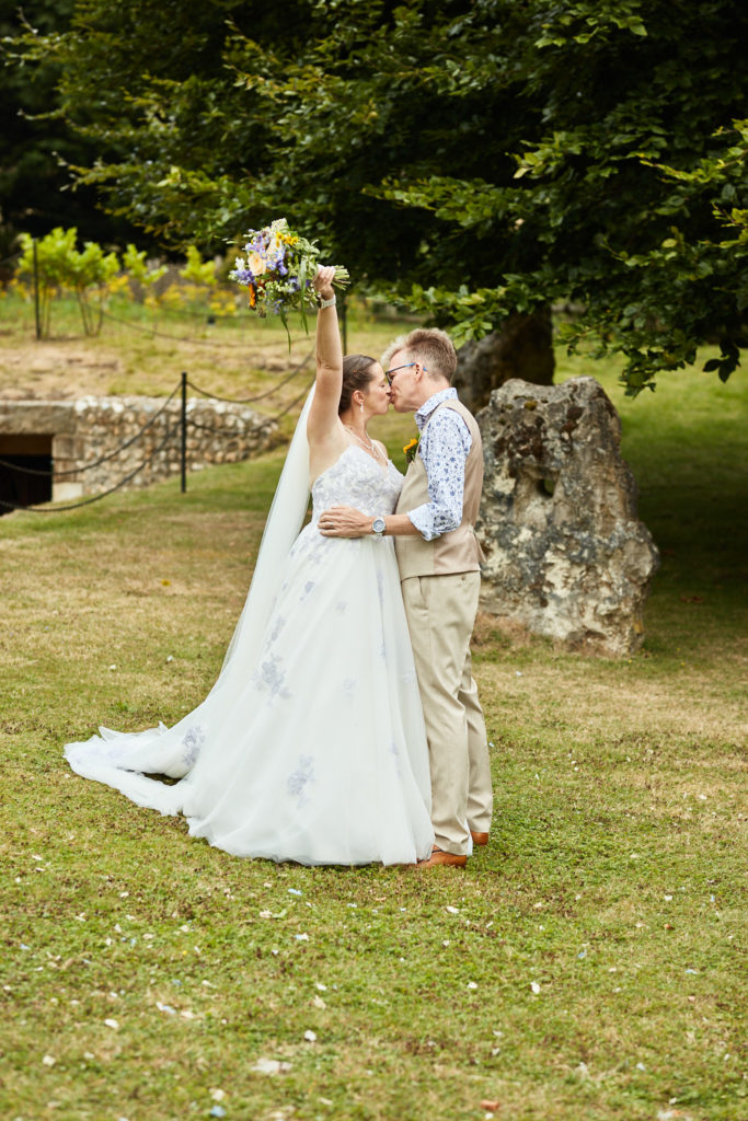 Bride holding her bouquet in the air as she kisses the groom on the lawn at Dode