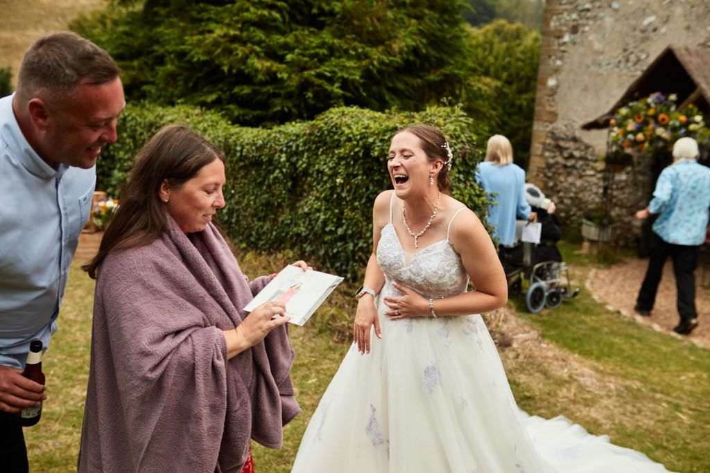 Bride laughing as a guest reads to her on the lawn