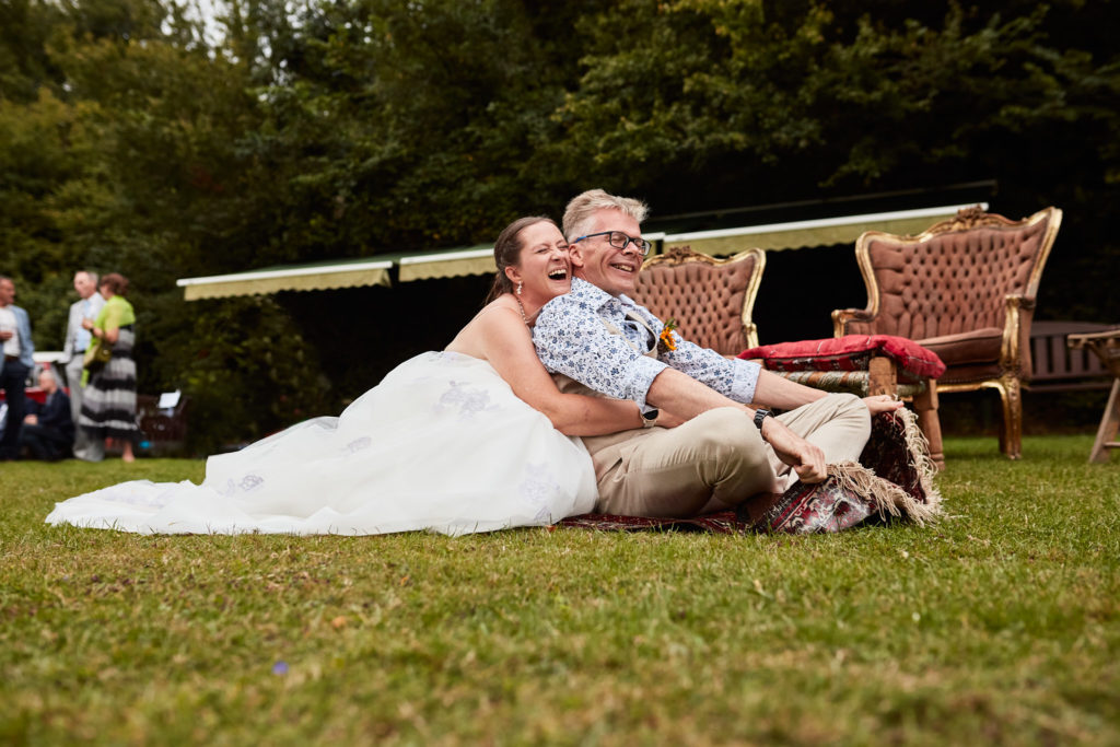 Bride and groom relaxing on cushions on the lawn at the Lost Village of Dode