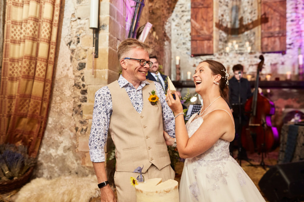 Bride laughing as she feeds the groom a piece of wedding cake