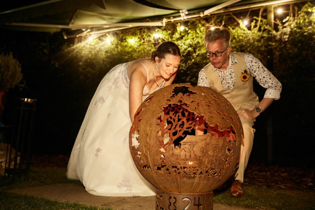 Bride and groom beside a globe-shaped fire pit at night