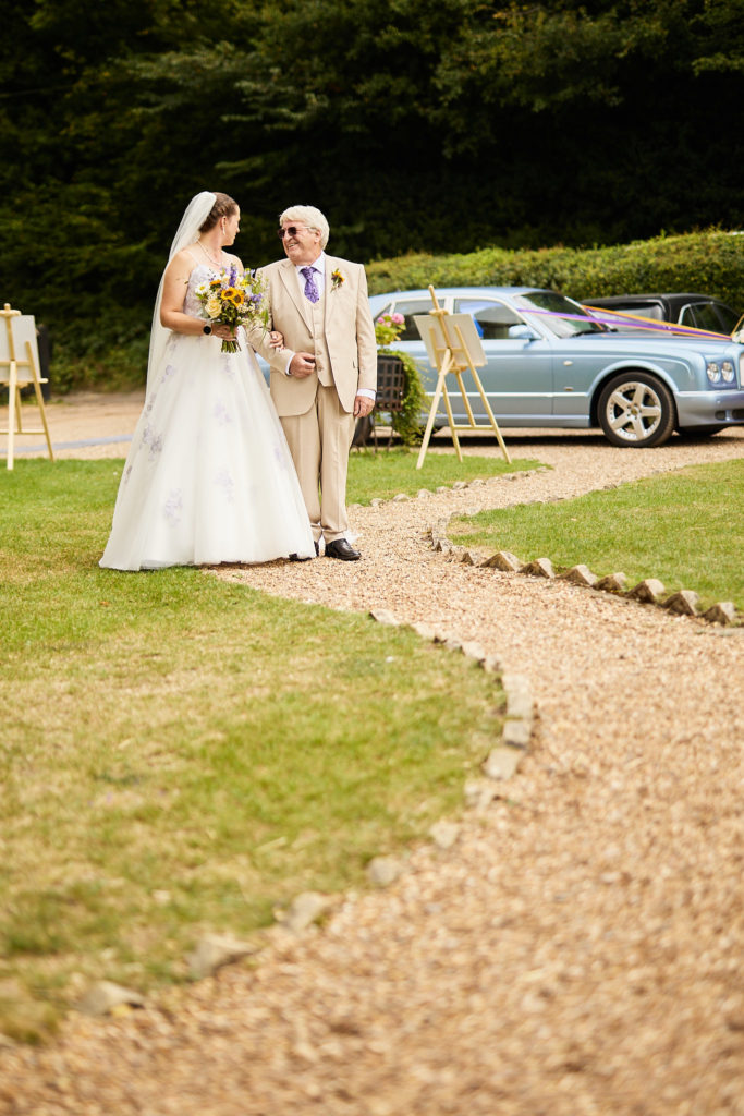 Bride and an elderly man in a cream suit walking up the path to the church