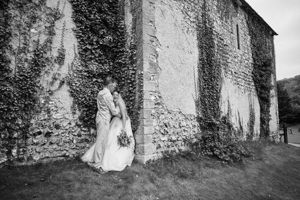Black and white photo of the bride and groom kissing beside the ivy-covered church at Dode