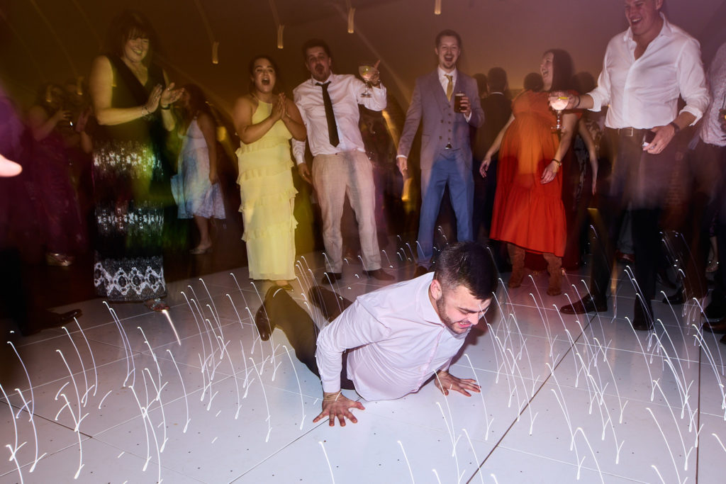 Wedding guest dancing down on the floor of the lit dance floor as others cheer