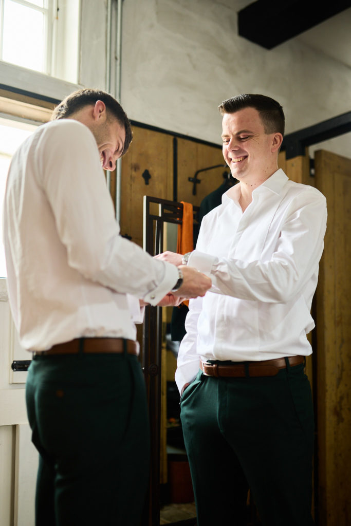 Groom and groomsman in white shirts getting ready, one fastening the other's cuff