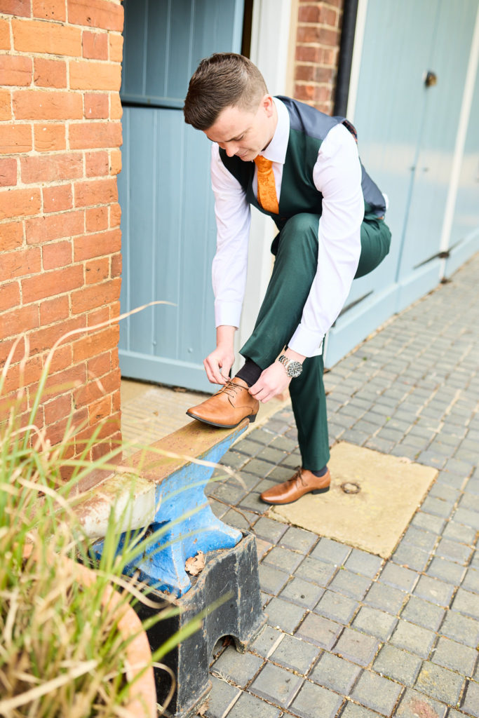 Groom in a green waistcoat tying his shoe on a doorstep