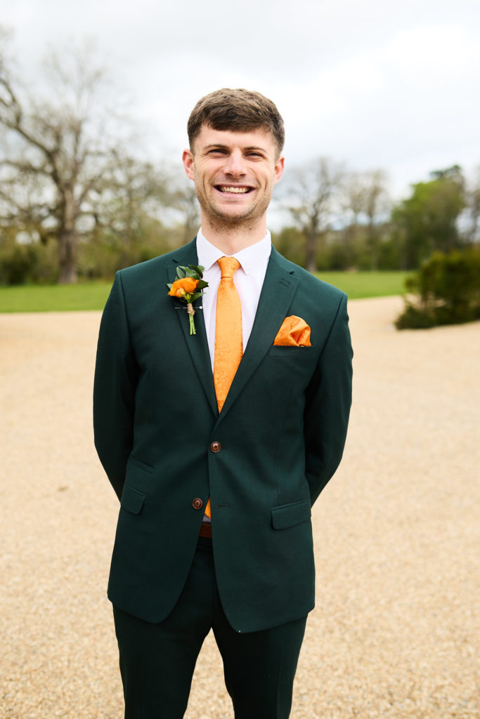 Groomsman smiling in a green suit with an orange tie