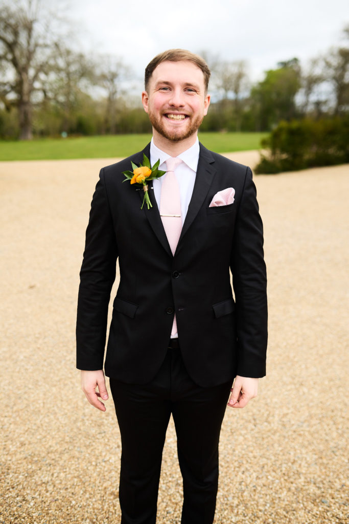 Groomsman smiling in a black suit with a pink tie