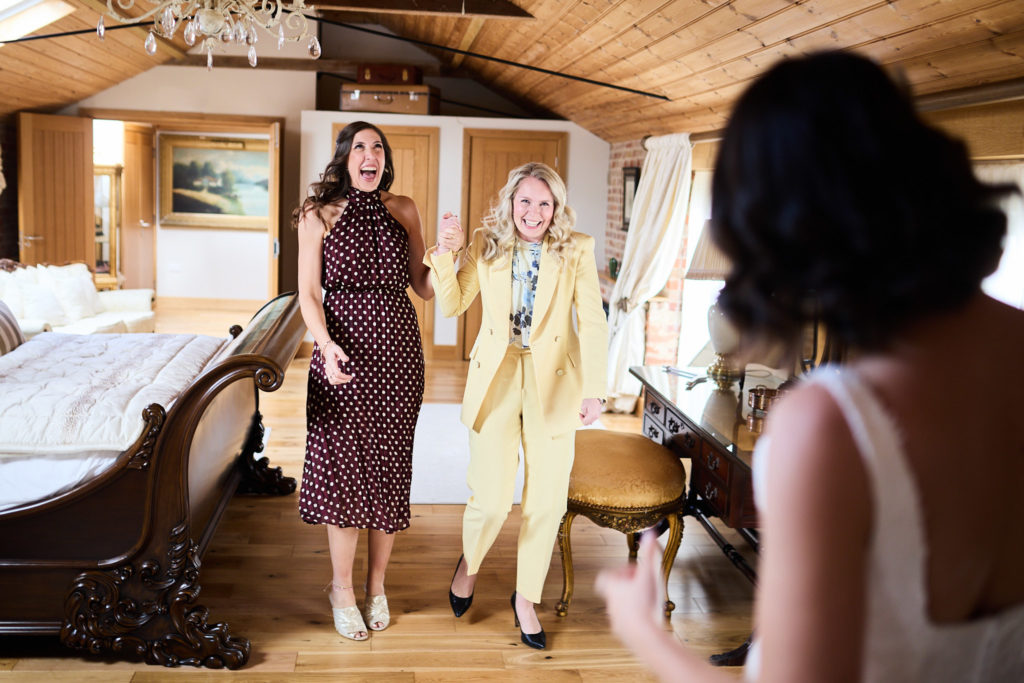 Two women reacting with delight as they see the bride in her dress