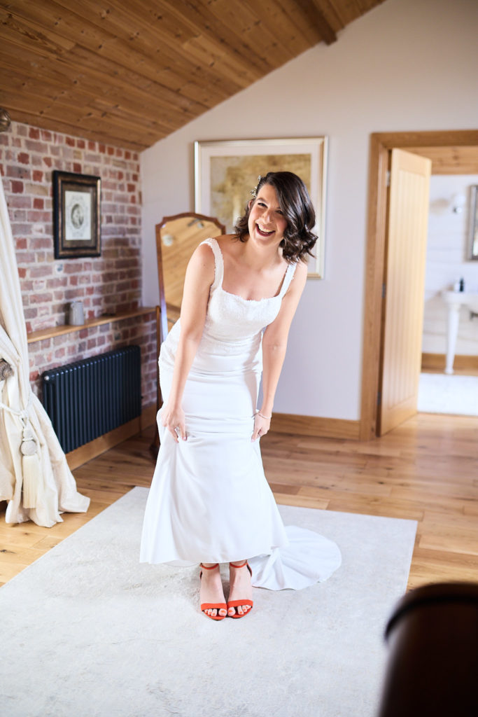 Bride laughing as she looks down at her orange shoes
