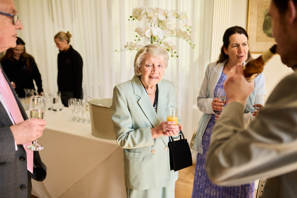 Older guest in a pale green jacket chatting with a drink in hand