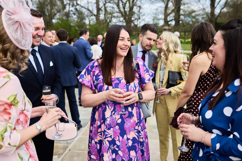 Wedding guest in a purple floral dress laughing among friends at the drinks reception