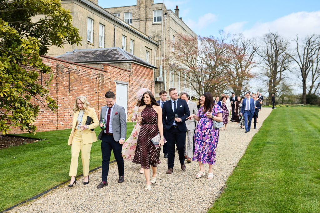 Wedding guests walking along the gravel path beside the walled garden at Hatfield Place