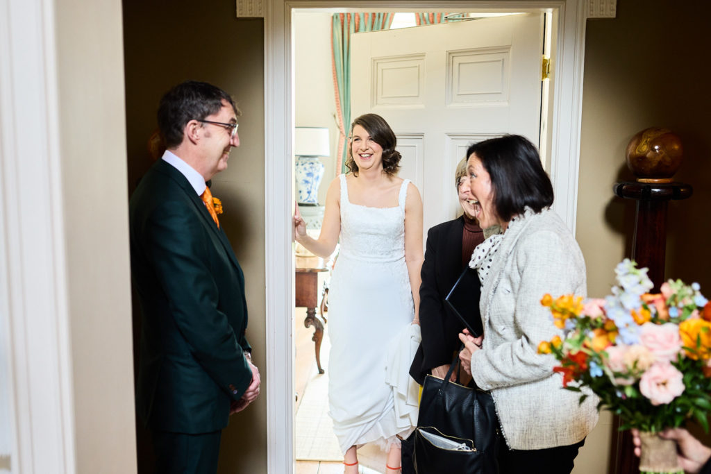 Groom waiting behind a doorway with the bride on the other side holding her bouquet