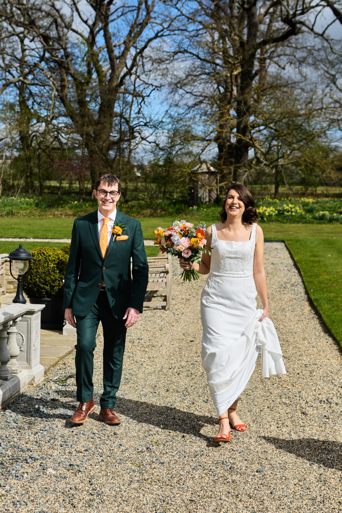 Bride and groom laughing as they walk hand in hand along the path at Hatfield Place, Essex