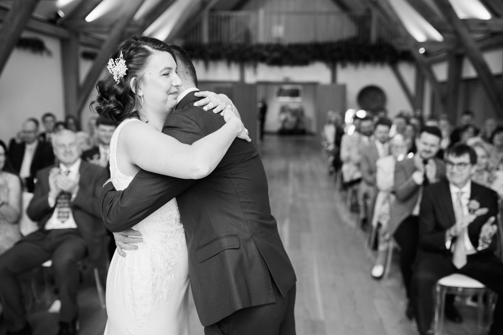 Black and white photo of the bride and groom hugging after the ceremony as guests clap