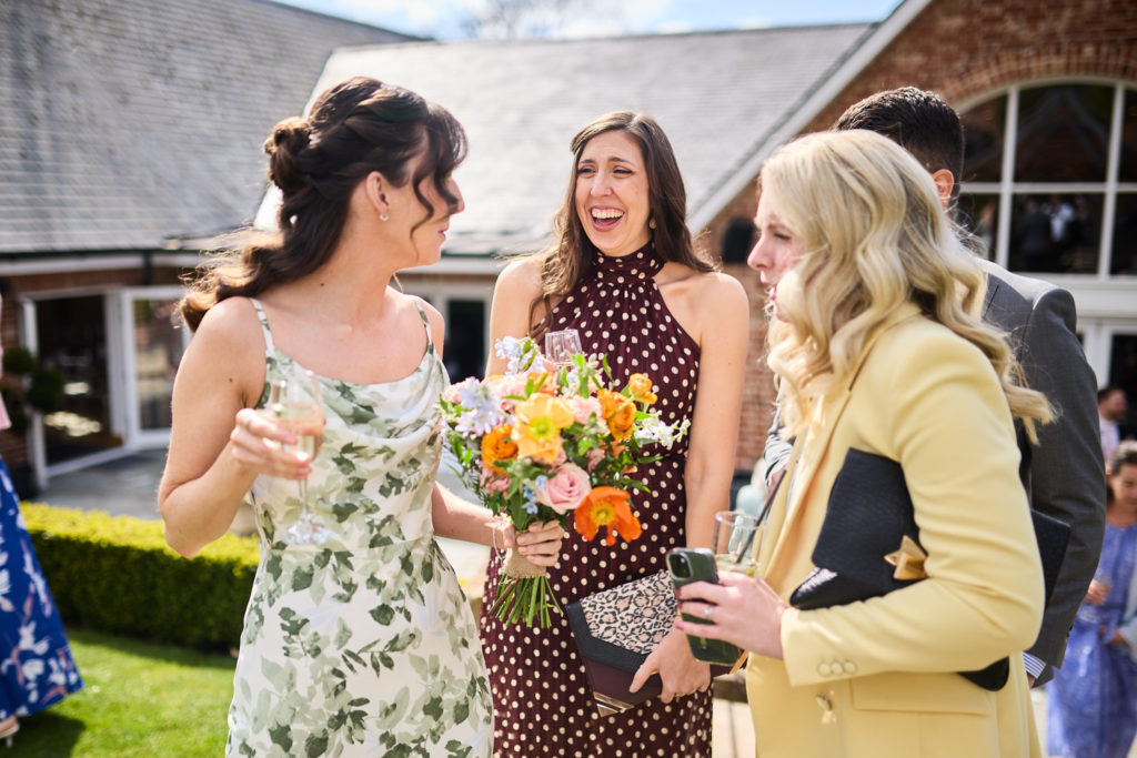 Bridesmaids chatting with drinks and bouquets in the sunshine