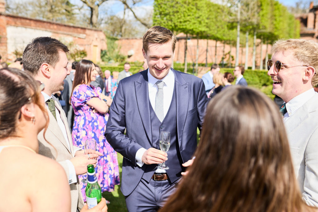 Wedding guest in a blue suit smiling with a drink among friends