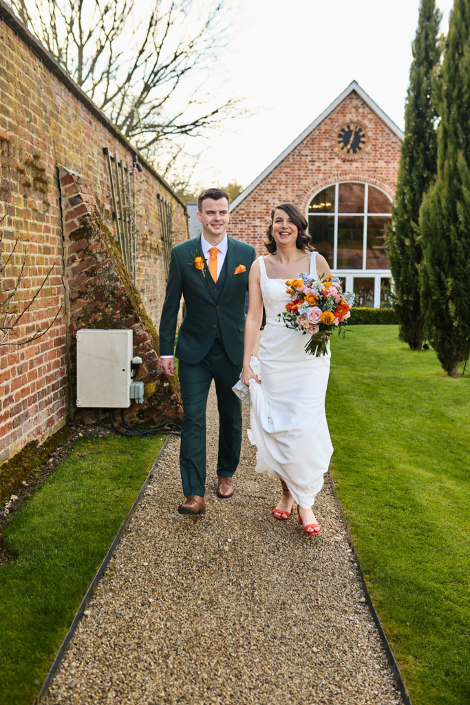 Bride and groom walking arm in arm along the path beside the clock barn at Hatfield Place, Essex
