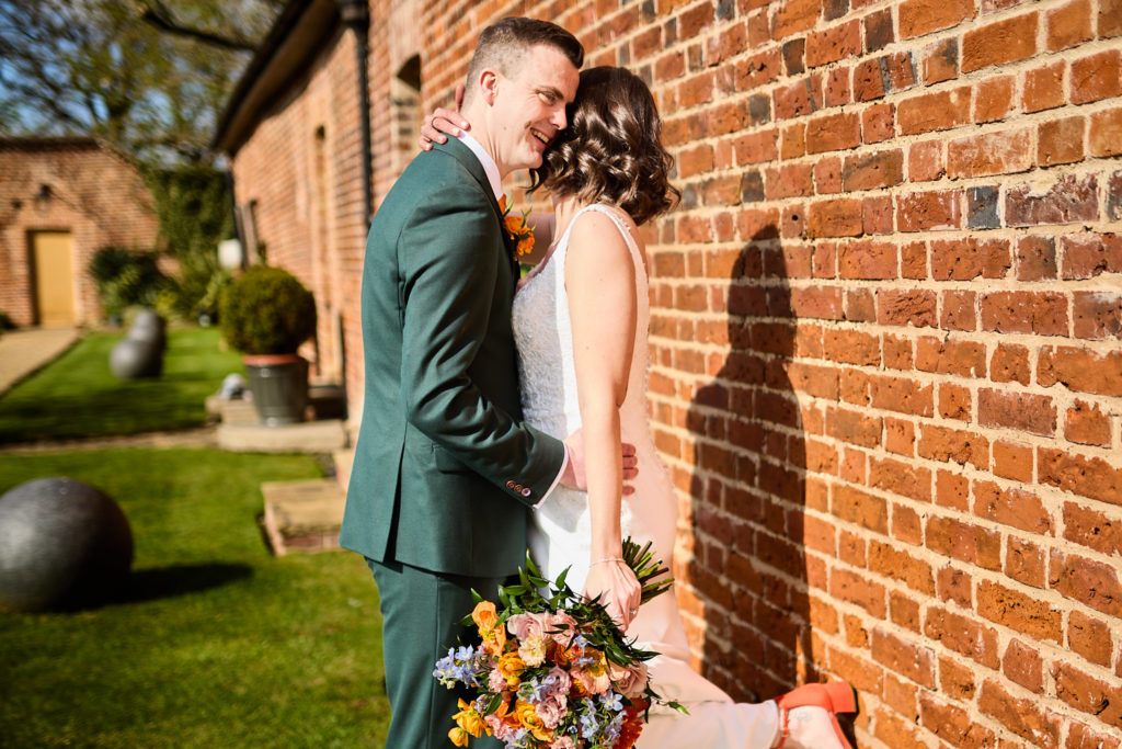 Bride and groom embracing against a red-brick wall at Hatfield Place, Essex