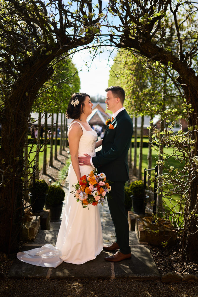 Bride and groom facing each other under a garden archway at Hatfield Place, Essex