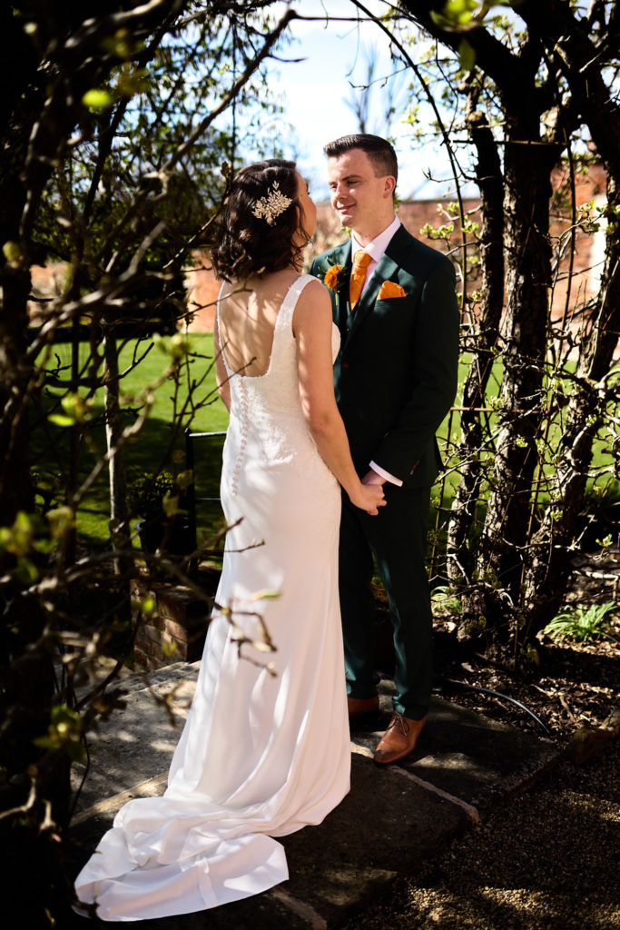 Groom smiling at the bride under an archway, her dress train trailing behind her, at Hatfield Place, Essex