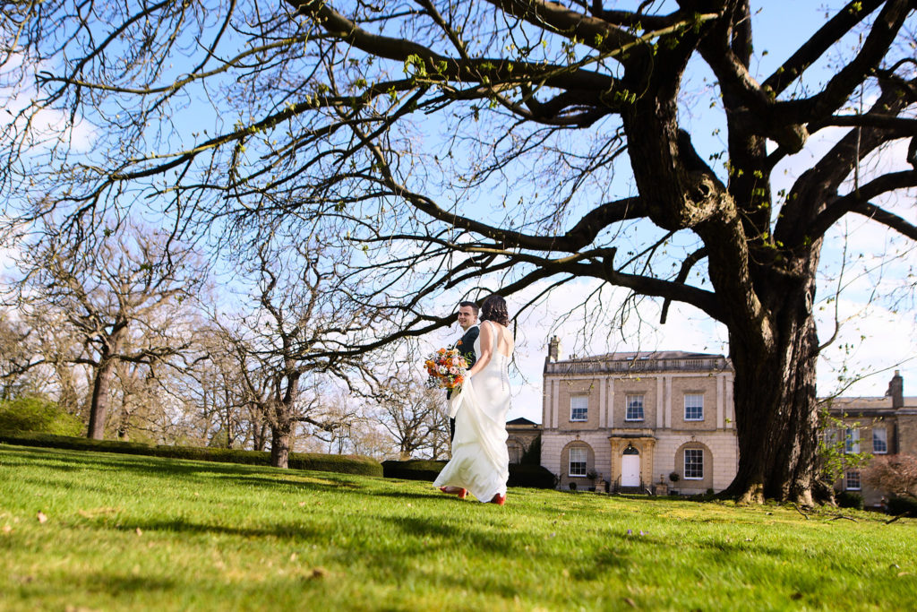 Bride and groom kissing under a large tree with Hatfield Place in the distance