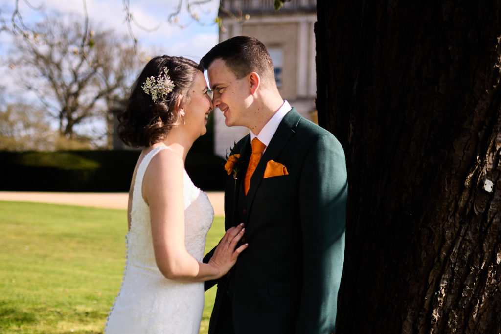 Bride and groom forehead to forehead beside a tree at Hatfield Place, Essex