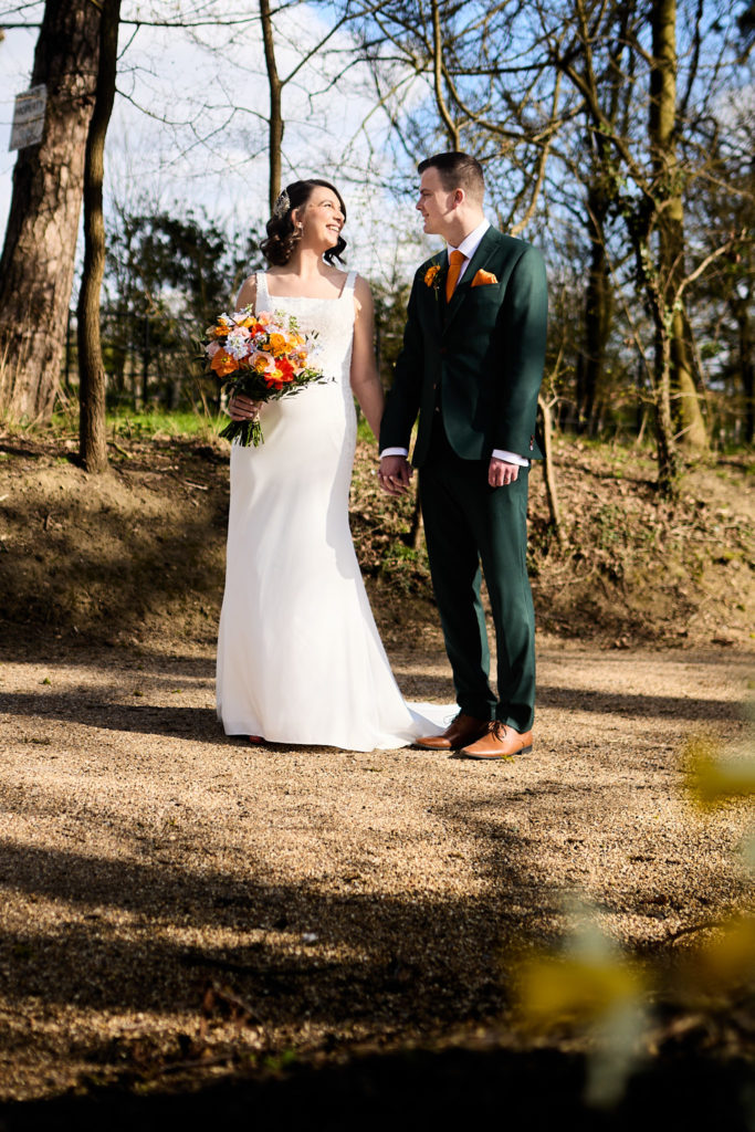 Bride and groom holding hands in dappled woodland light at Hatfield Place