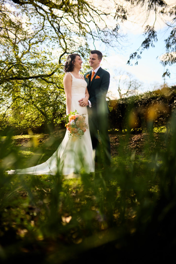 Bride and groom seen through foliage at Hatfield Place, her dress train spread out