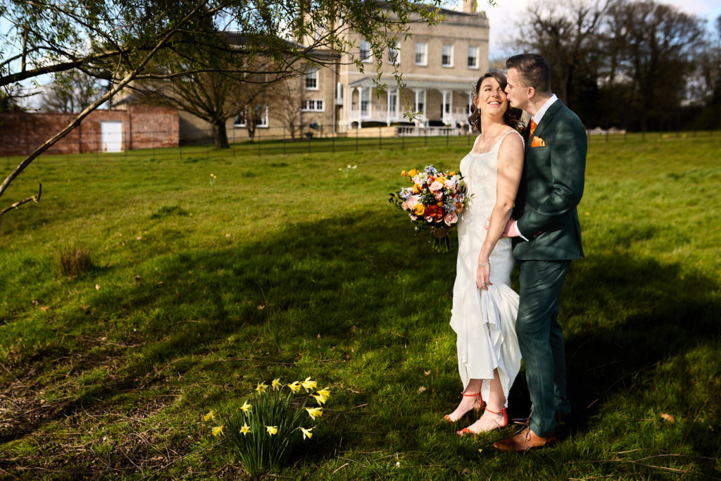 Bride and groom kissing on the lawn in front of Hatfield Place, Essex