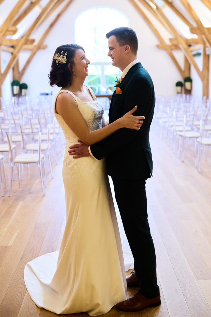 Bride and groom laughing in each other's arms in the oak-beamed barn at Hatfield Place