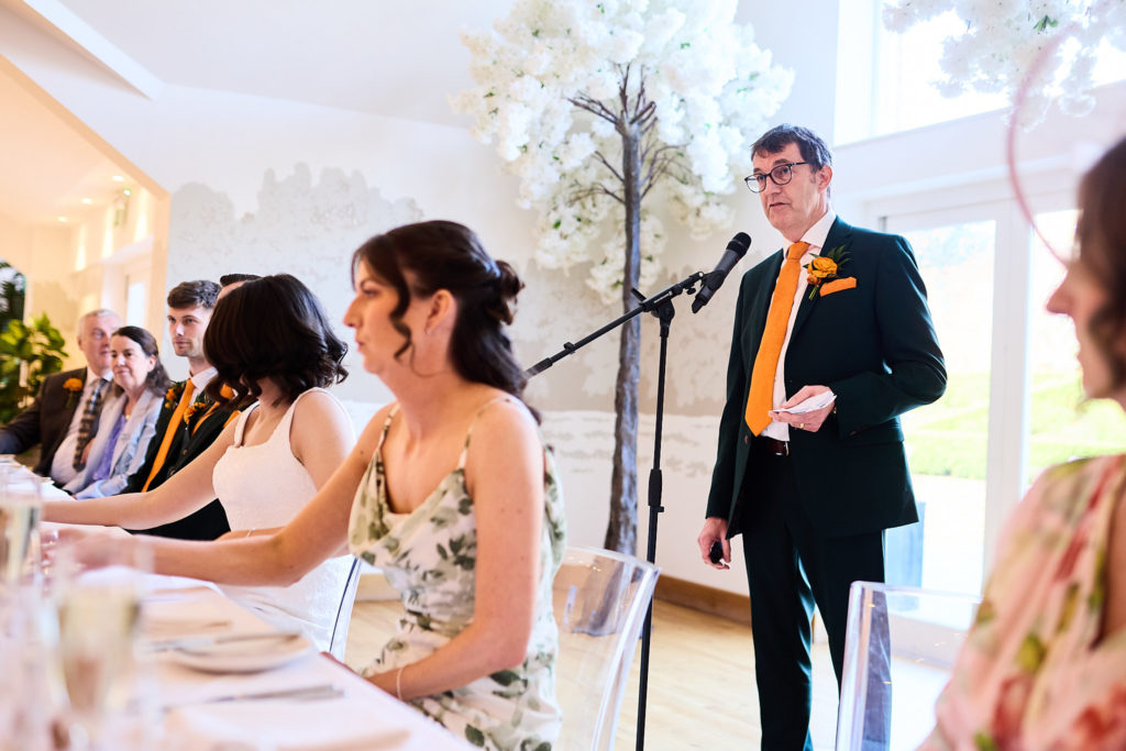 Groom giving his speech at the microphone as the bride and guests listen