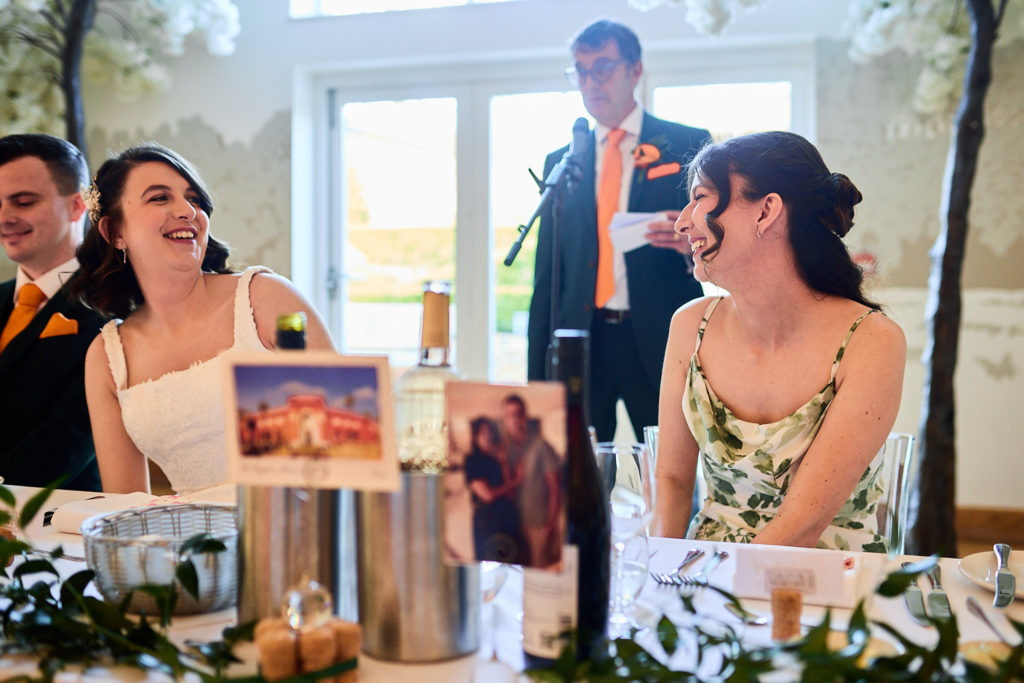 Bride and bridesmaid laughing at the top table during the groom's speech