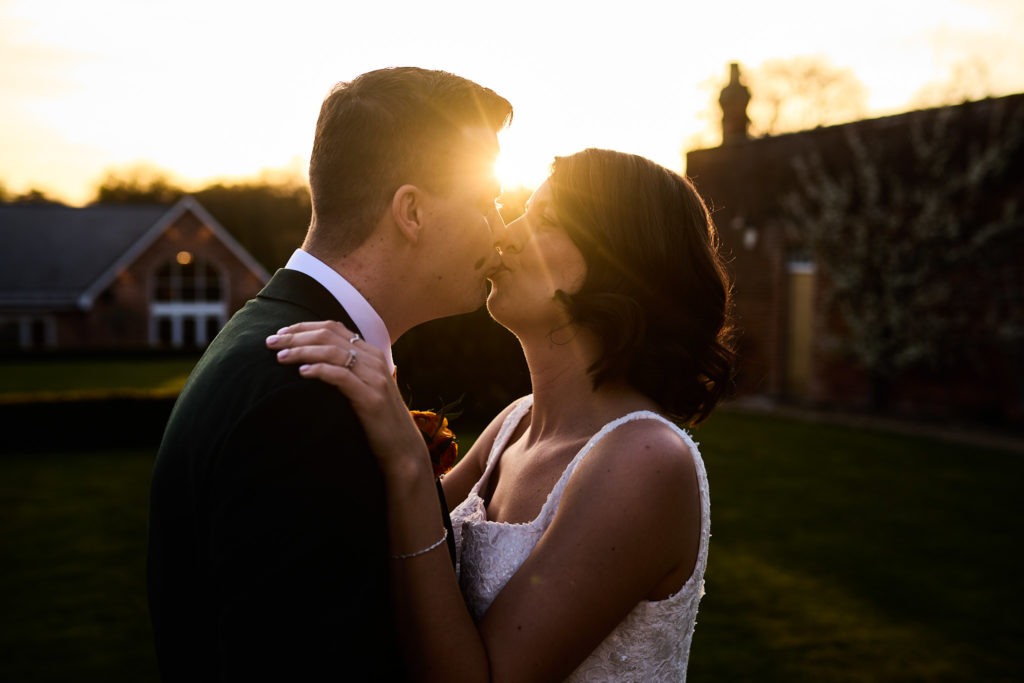 Bride and groom kissing at sunset with the sun flaring between them at Hatfield Place